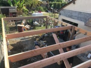 Un charpentier réalise une charpente en bois dans une arrière-cour du 49ème région.
